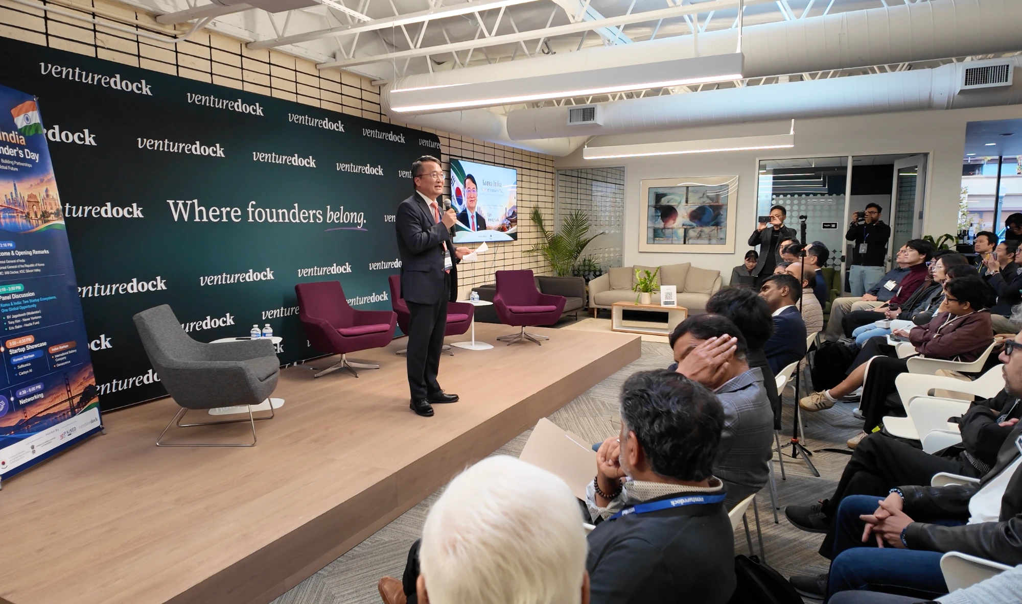 A speaker gives opening remarks on the Venture Dock stage in Palo Alto in front of a seated audience